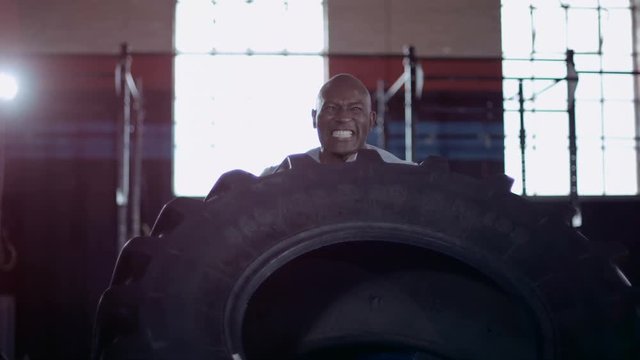  Muscular African American man cross training with tractor tyre at the gym