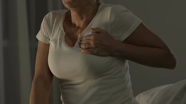 Retired woman sitting on couch and suffering from heart attack, health problems
