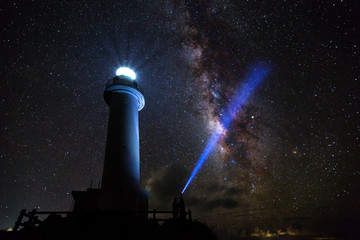The Uganzaki Lighthouse at night with the Milky Way behind it and a bright laser light shining up in Ishigaki, Japan