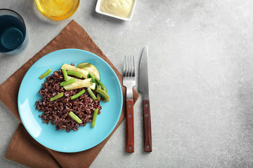 Plate with red rice and vegetables on table
