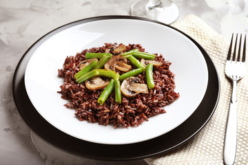 Plate with red rice and vegetables on table