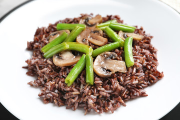 Red rice with mushrooms and green beans on plate, closeup