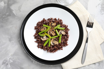 Plate with red rice and vegetables on table