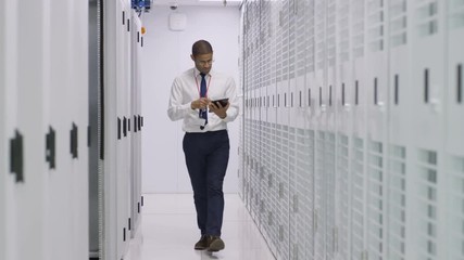 IT engineer with computer tablet checking the servers in a data center. Two businessmen taking a look round in the background.