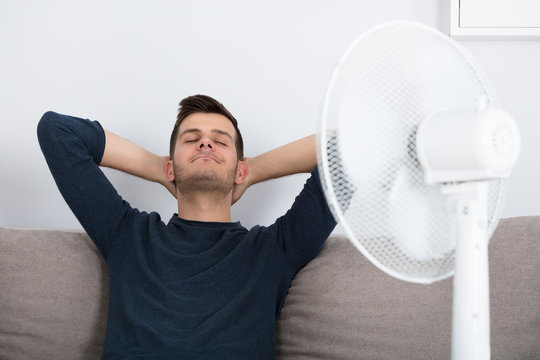 Man Sitting On Couch Cooling Off With Fan