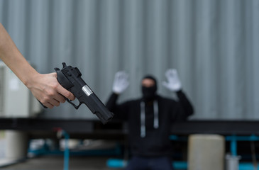 Young woman holding handgun self defense from bandit man, villain or thief stood with mask