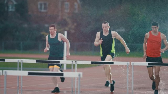  Athletes training at the track, running & jumping over hurdles in the rain