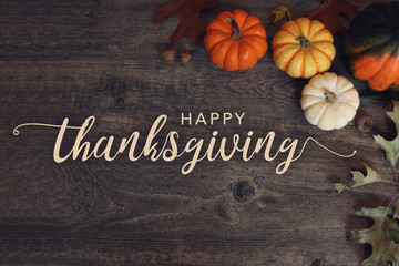 Happy Thanksgiving text with pumpkins and leaves over dark wood background - Powered by Adobe