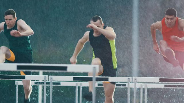  Athletes running & jumping over hurdles at athletics track in the rain