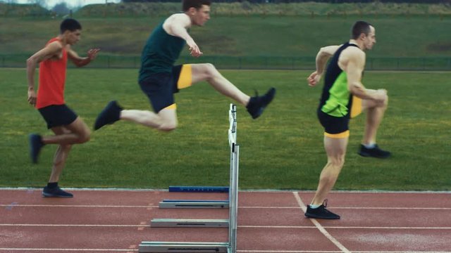  Competitive athletes running & jumping over hurdles at athletics track