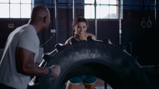 Woman and her fitness instructor cross training with tractor tire at the gym