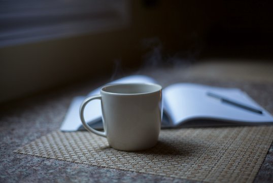 Cup of steamy hot coffee with a notebook beside it