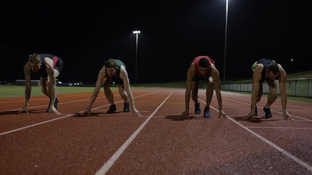  Competitive male athletes running at race track in the dark. Slow motion.