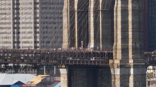 A long establishing shot view of pedestrians and tourists on the Brooklyn Bridge walkway.  	