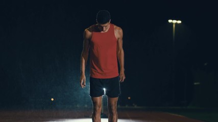  Male athlete training at running track in the dark & in the rain. Slow motion