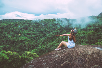 Asian women travel relax in the holiday. sit on a rocky cliff. Wild nature wood on the mountain.