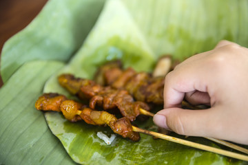 Girl child hand take toast pork stick with a piece of sticky rice on banana leaf, Thai food or street food