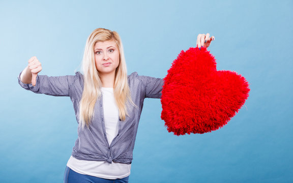 Woman holding red heart showing thumb down