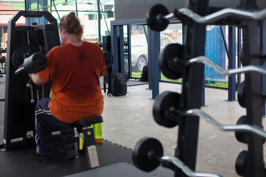 An overweight man exhausted with exercising in fitness center.