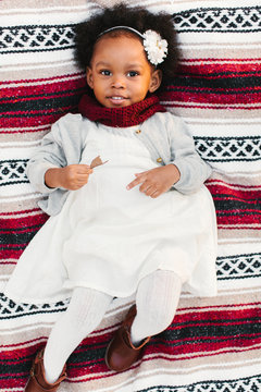A little African American girl laying down on blanket.