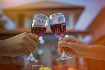 Man hand and woman hand holding a glass of red wine to celebrate Christmas and New Year. The back of the house is a bokeh of light. In the evening when entering the winter.