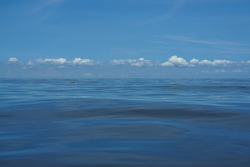 Natural background scene of gradient blue sky horizon and low raining white cloud above deep blue sea moving water ripple freezing motion with reflection