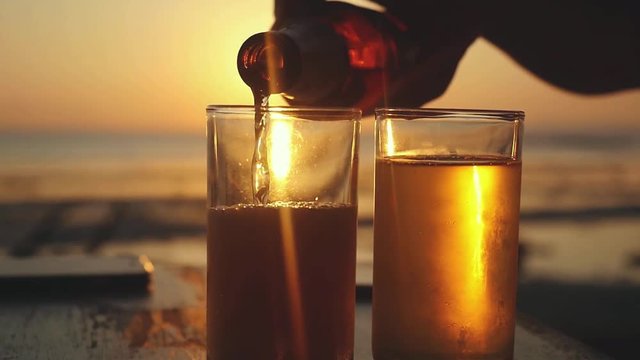 Pouring Beer in a Glass on a tropical Beach at beautiful Sunset with lens flare effects in slow motion. 1920x1080