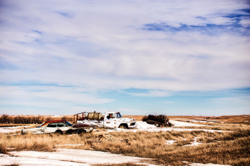 An old white truck and four door gray rusty car abandoned in a snow dusted field in a rural winter landscape