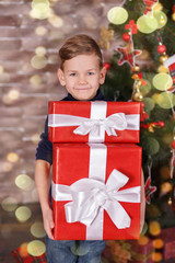 Handsome cute boy celebrating New Year Christmas alone close to xmas tree on red pillow posing in studio decoration wearing jeans and blue shirt with jazzbow tie