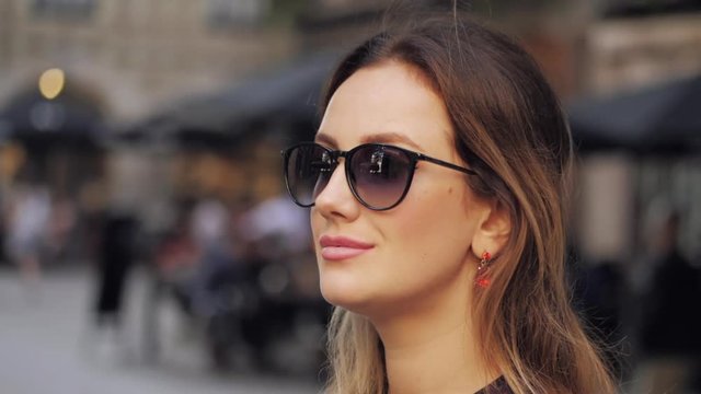 Charming young woman with a magnificent golden hair, gorgeous pink lipstick and stylish look. Attractive young lady in black sunglasses standing in european street. Slow motion