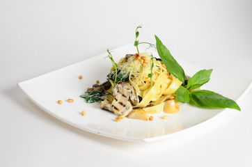 Fettuccine with mushrooms, spinach and pine nuts in creamy sauce on a plate on white background