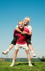 Cute senior Couple: doing sports / Fitness: jogging against clear blue Sky Piggy Back