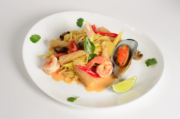 Pasta tom yam with seafood and vegetables on a plate on white background