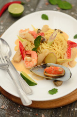 Pasta tom yam with seafood and vegetables on a plate  with fork and spoon on wooden background