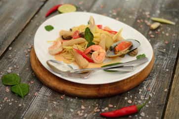 Pasta tom yam with seafood and vegetables on a plate  with fork and spoon on wooden background