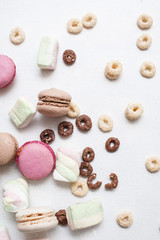 Colorful sweets on white background top view. Delicious macaroons, zephyrs and corn flakes are spread around, close up