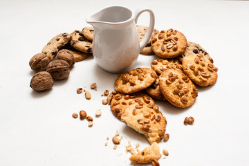 Culinary background of organic pastry shop. Wholegrain scone with peanuts and chocolate laying around pitcher of milk on white table. Concept of delicious breakfast with cookies