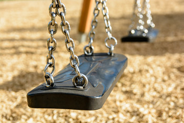 Close-up view of a still child's swing in black plastic in a wood chips covered playground with...