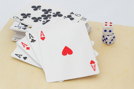 Four aces in front with stack of playing cards at the back with dices on the table. Isolated white background.
