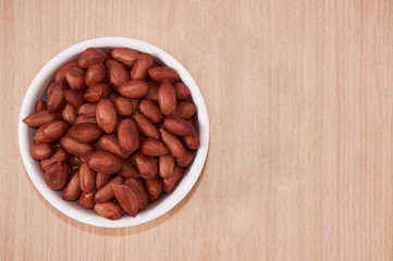 Peanuts in a white bowl. Against the background of a light tree. Top view.