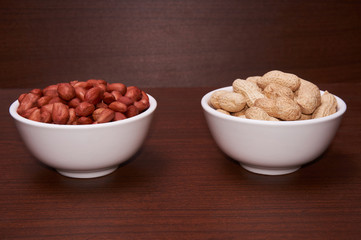Peanuts in a white bowl. Against the background of a dark tree. Side view.