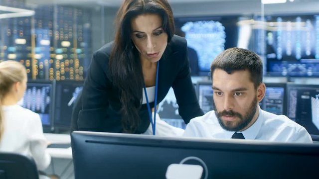 Female Chief Computer Engineer Consults Male Neural Network Architect. They Work in a Crowded Office on a Neural Network.