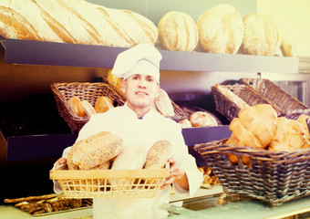 Male employee offering fresh baguettes and buns in bakery