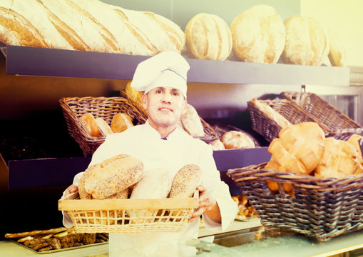 Male employee offering fresh baguettes and buns in bakery
