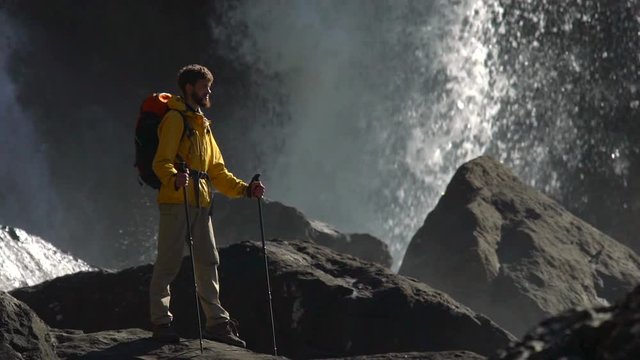 A male hiker watches a big waterfall in slow motion.