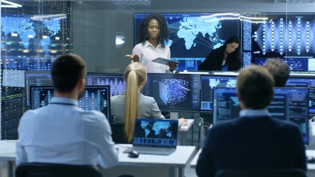 Chief Project Engineer Consults Tablet Computer and Holds Briefing for a Team of Scientists that are Building Machine Learning System. Displays Show Working Model of Neural Network. 