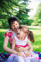 Portrait of joyful disabled girl who sitting on the laps of her happy mother outdoors