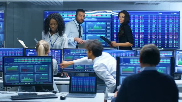 Multi-Ethnic Team is Busy Working at the Stock Exchange Office. Traders and Brokers Buy and Sell Stocks on a Market. Monitors Display Relevant Infographics, Data and Numbers.