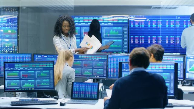 Multi-Ethnic Team of Traders is Busy Working at the Stock Exchange Office. Dealers and Brokers Buy and Sell Stocks on the Market. Monitors Display Relevant Infographics, Data and Numbers.