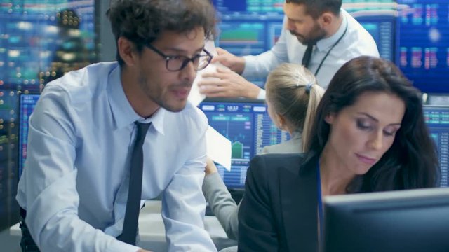 Professional Broker Consults Stock Exchange Trader at Her Workstation. Multi-Ethnic Team at Stock Exchange Office is Busy Selling and Buying Stocks on the Market. Displays Show Relevant Data Numbers.